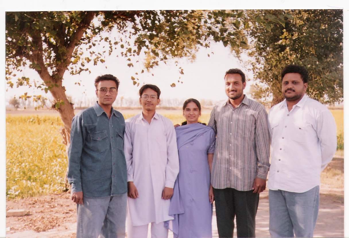 5 people pose under trees and in front of a farm