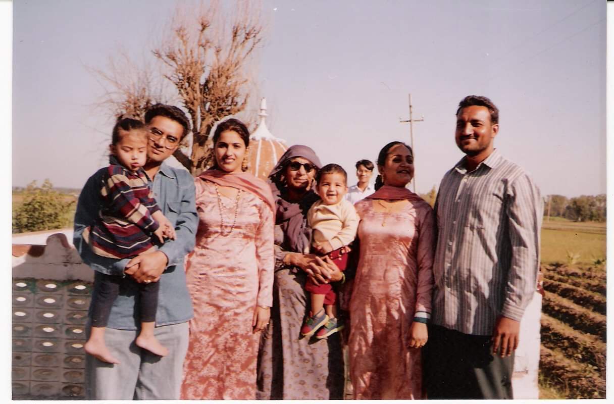 5 adults and 2 children stand in front of a farm.