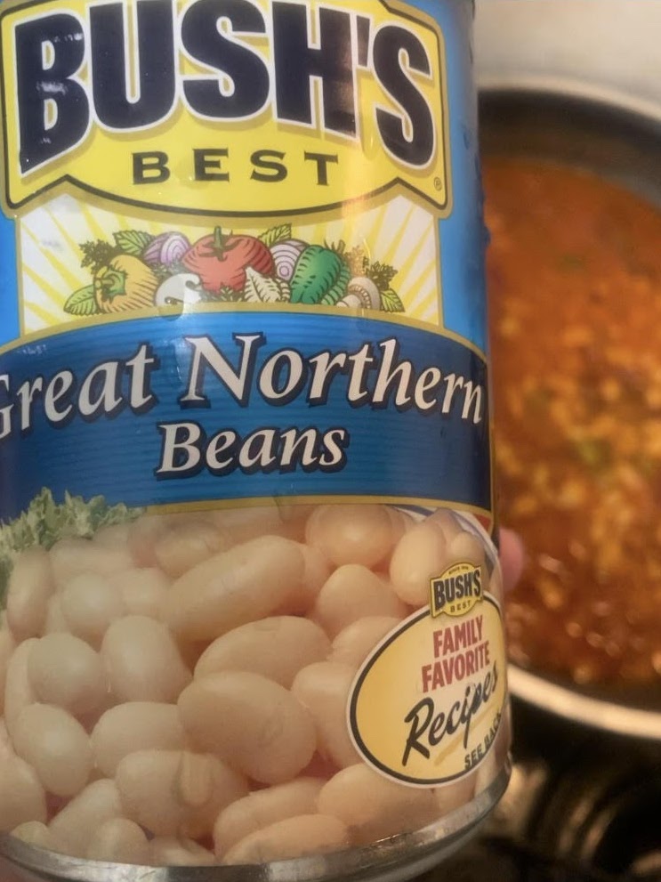 Can of white beans in foreground. Reads "Bush's Best Great Northern Beans." Beans cooking in background.