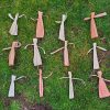 Eighteen cornhusk dolls lay on grass. Half of them are dyed slightly pink, the rest are plain. They alternate by color.