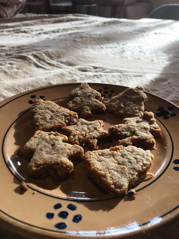 Star, bell, and tree shaped cookies are plated on a white table cloth.